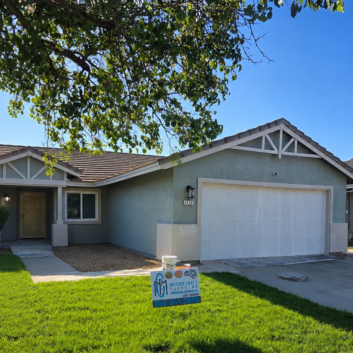 Single-story home before, with faded sage-green stucco